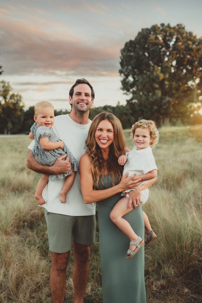 Parents holding two toddlers in an open field at sunset during a Greensboro fall family photo session