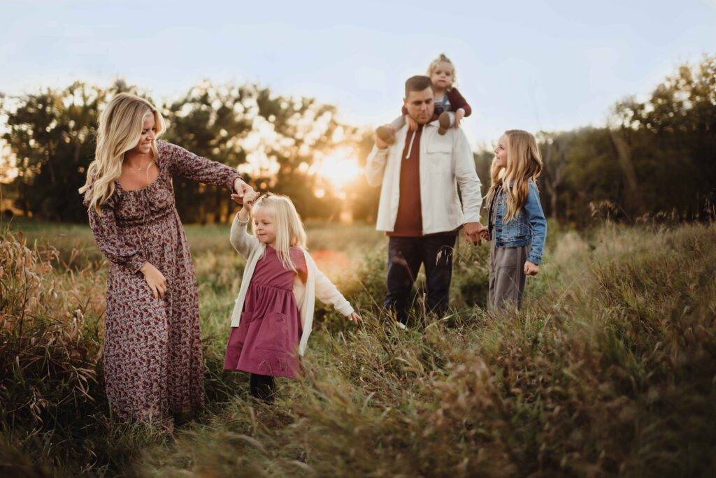 Family of five walking through a field at sunset during a fall Triad family photography session. 