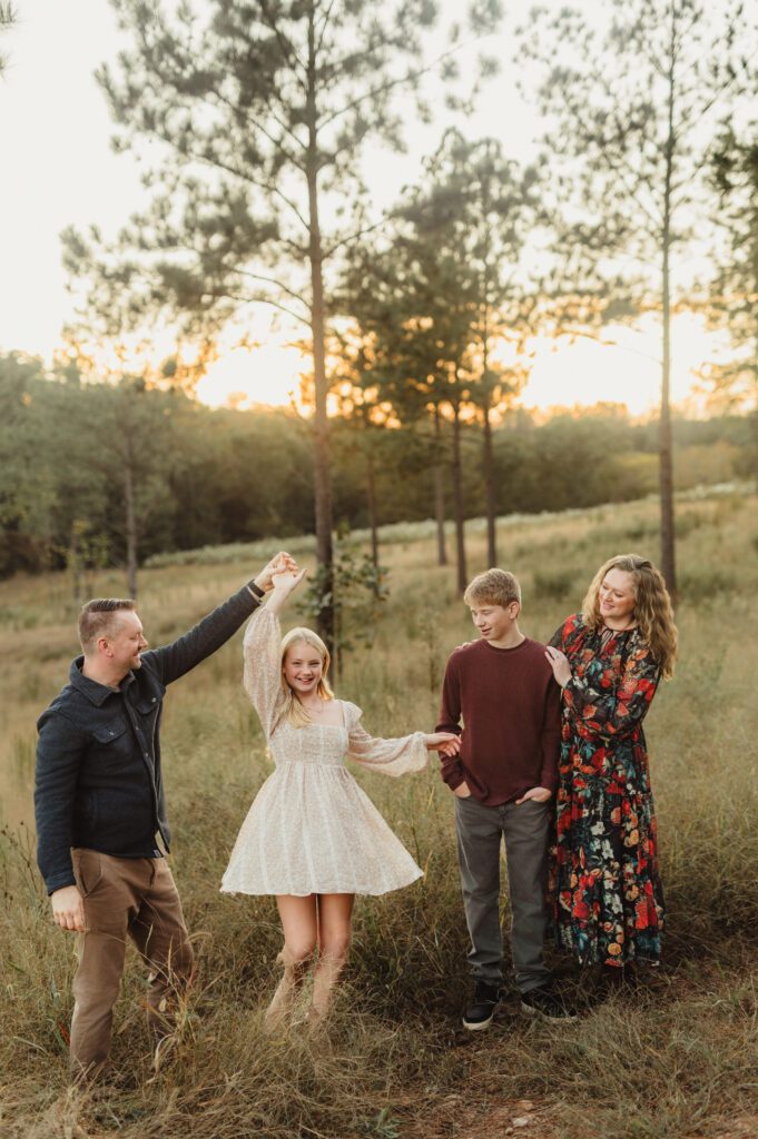 Family of four dancing together in a sunlit field with two teenagers during a Greensboro fall family photo session