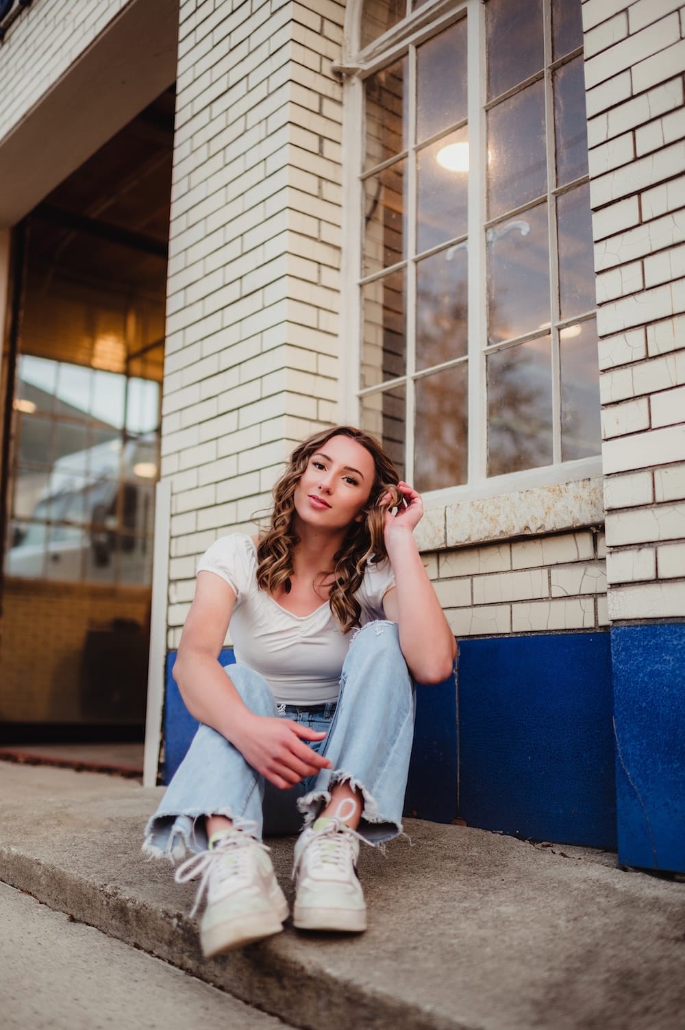 Senior girl in denim and a white top sitting on a downtown Greensboro stoop, a classic senior session outfit idea