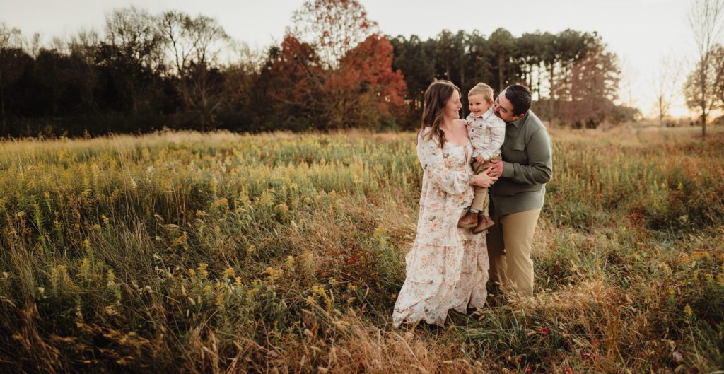 Parents cuddling their toddler son in a field at sunset during a Triad fall family photography session