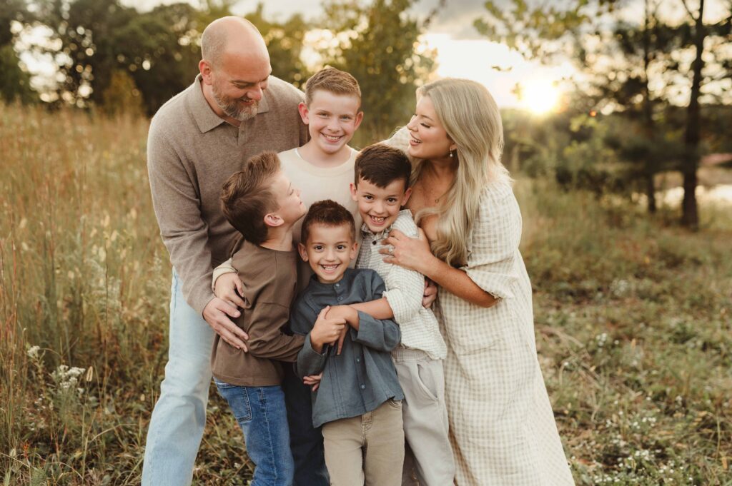 Family of six (four sons!) embracing and laughing together in a sunlit field during an NC fall family photo session