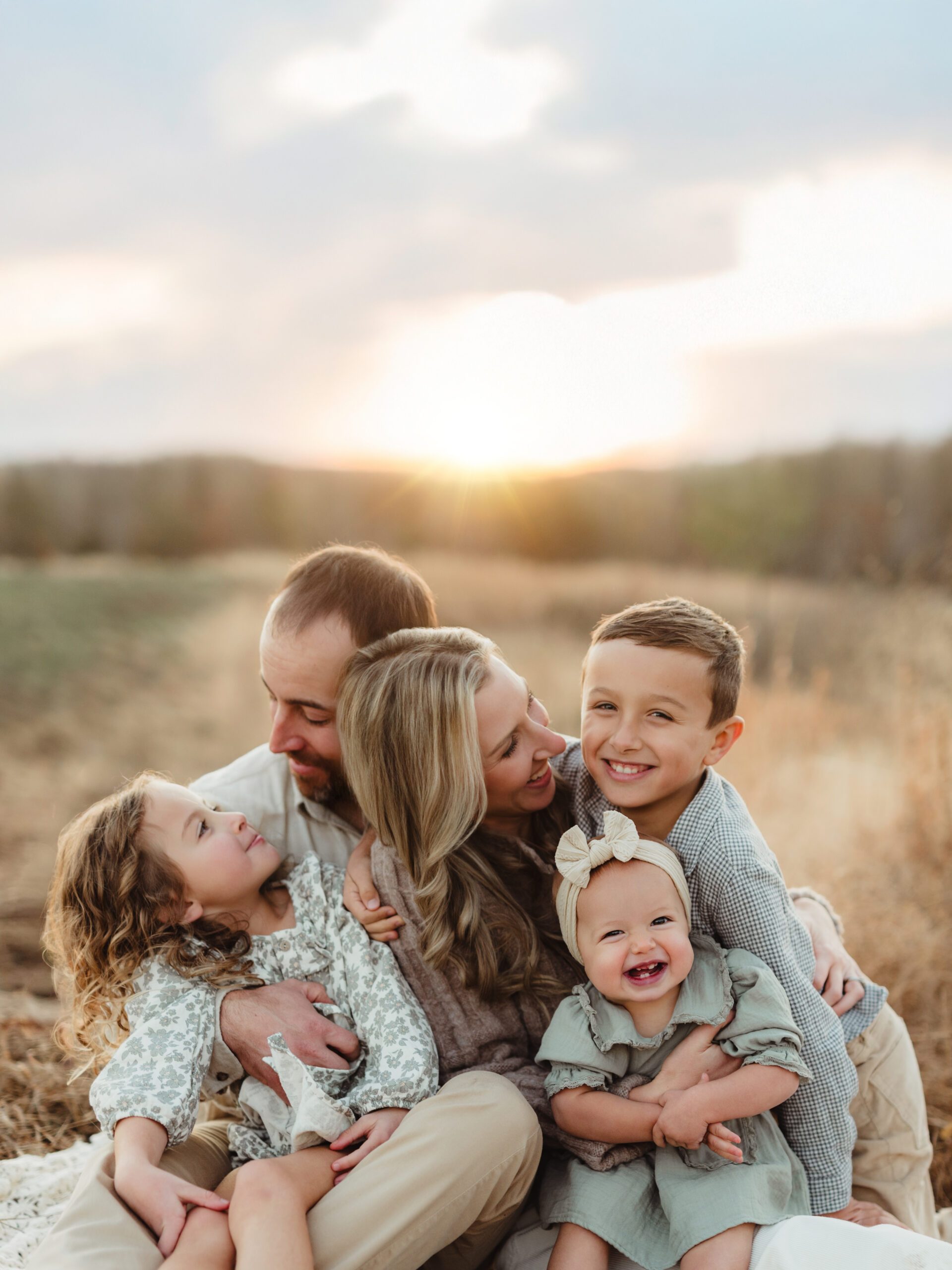 Family of five cuddled together on a blanket in a golden field at sunset during a Triad fall family photo session