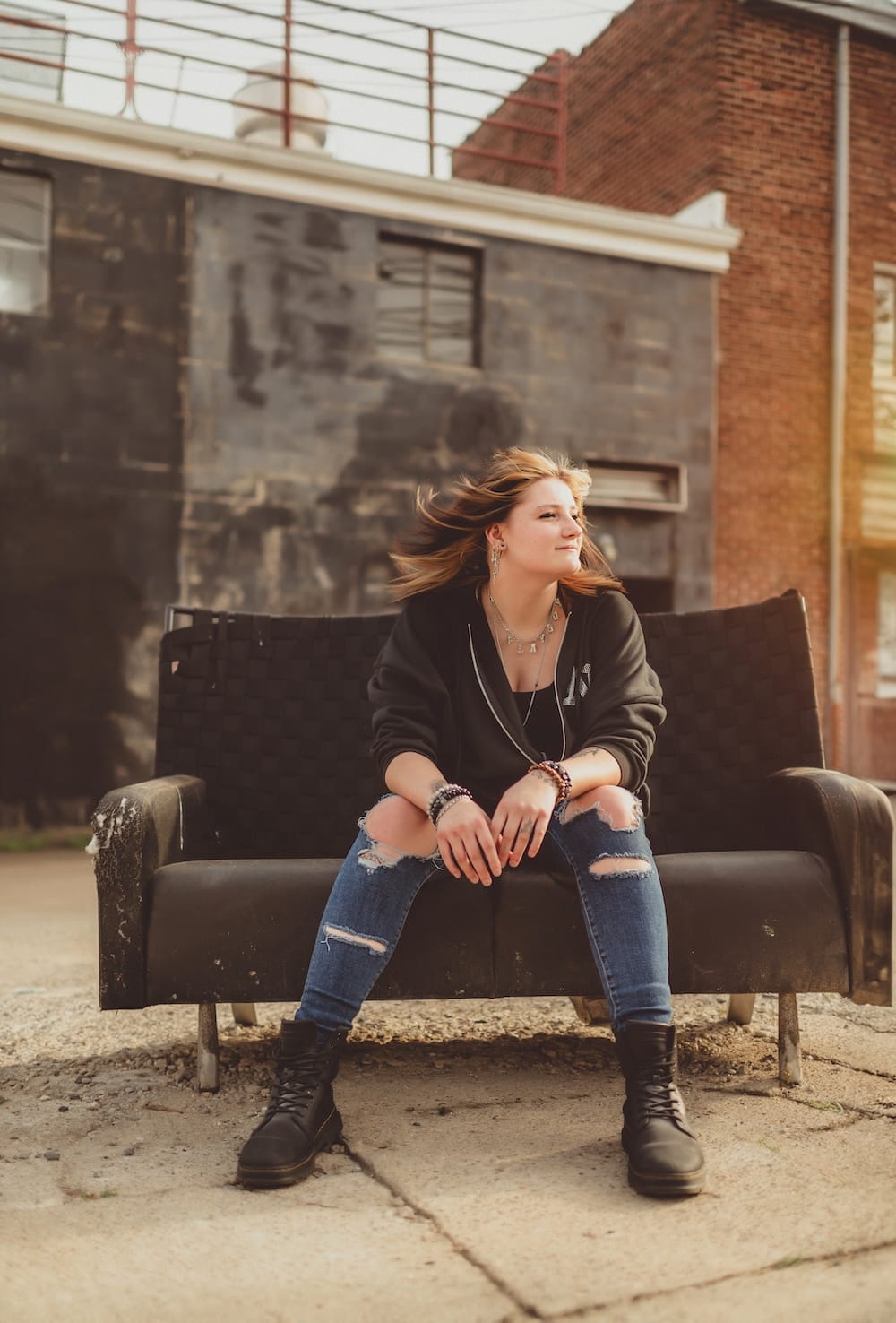 Senior girl in a leather jacket and ripped jeans sitting on a vintage couch in a downtown alley, an edgy senior session outfit idea