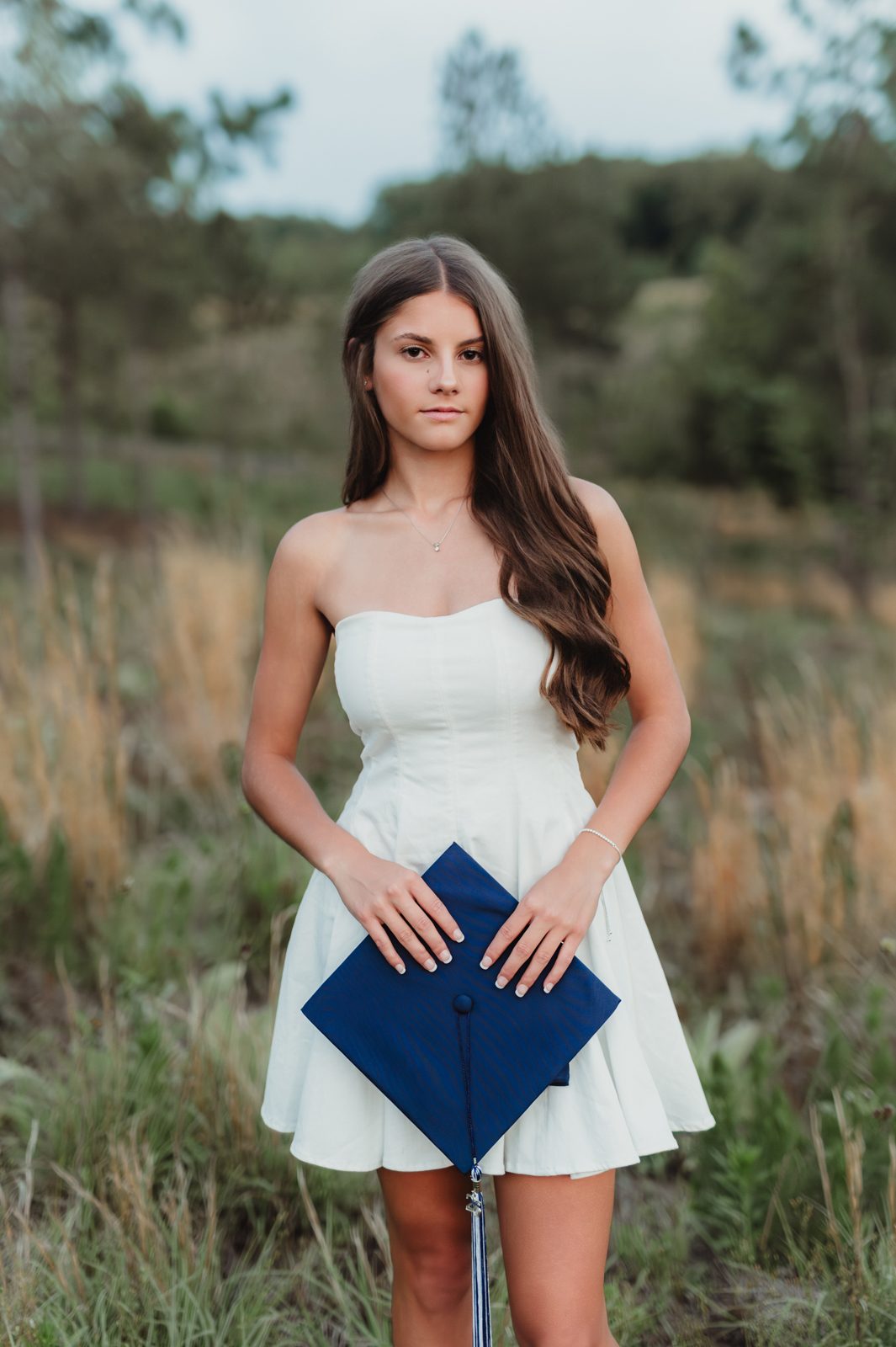 Greensboro graduation photos, senior in white dress holding her navy graduation cap in front of her