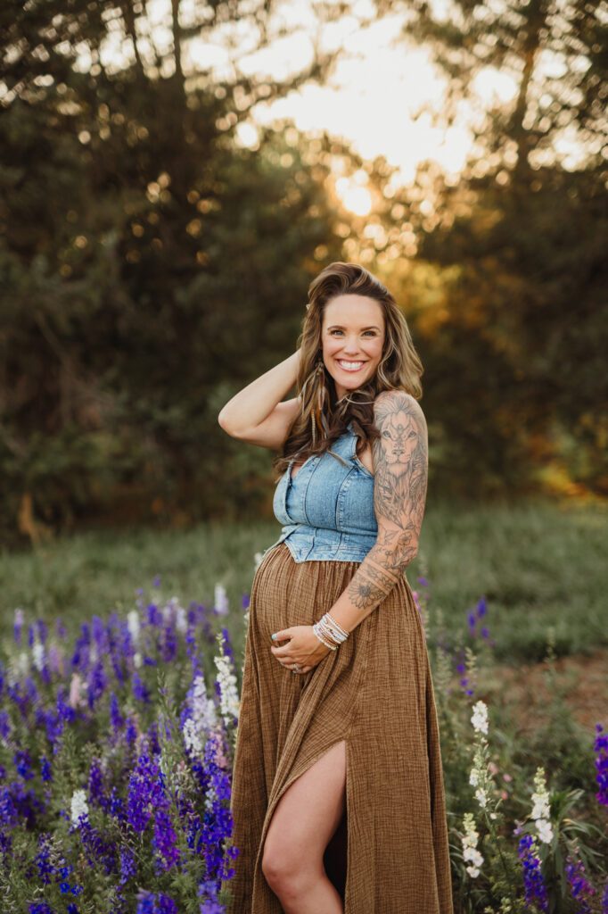 Worth the Drive: A Wake County Wildflower Session with the McInnes Family Pregnant mom in a denim top and brown maxi skirt, smiling and cradling her belly in a wildflower field