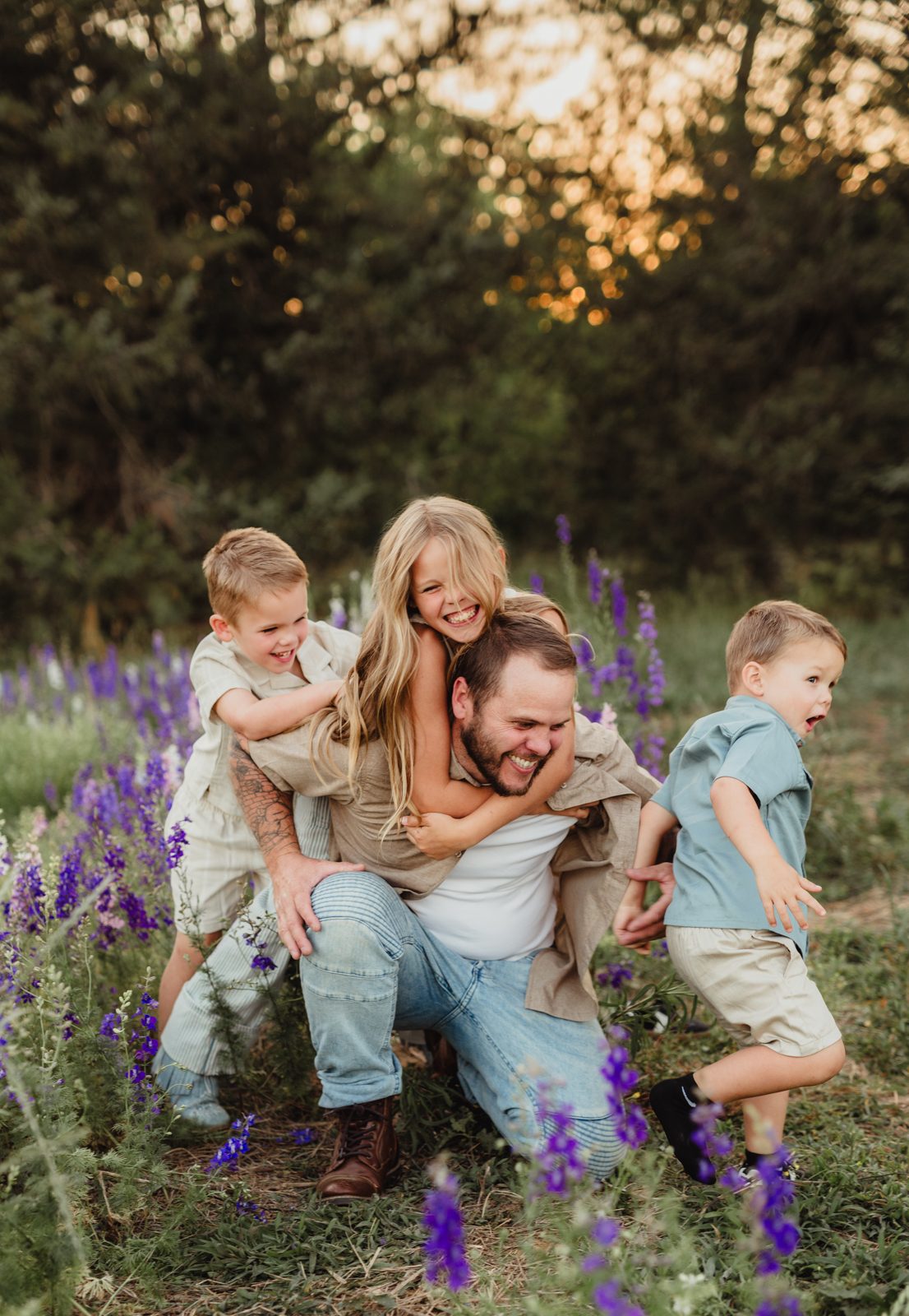 Worth the Drive: A Wake County Wildflower Session with the McInnes Family Dad giving his daughter and two sons a piggyback ride while they laugh and run through a wildflower field